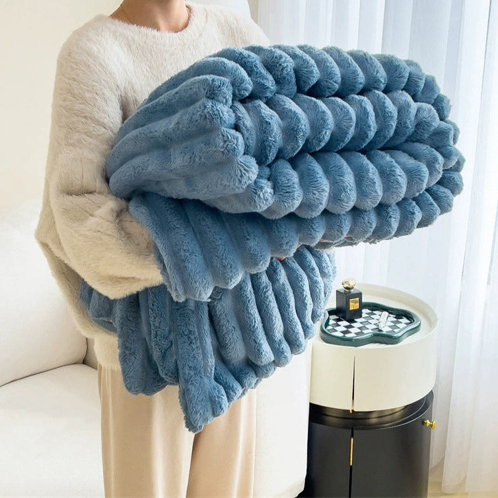 Person holding a blue fluffy blanket in a room with a white curtain and a small table.